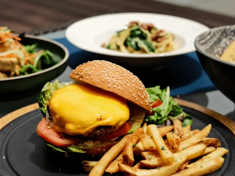 A plate of hamburger and fries together with plates of pasta and salad