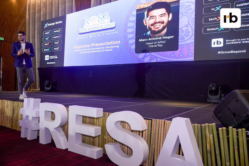 A man stands on stage before a large screen displaying "RESA," representing the Retail & Ecommerce Summit Asia.